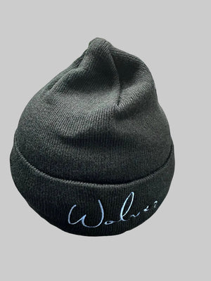 A black ribbed knit beanie with 'Wolves' embroidered in light blue script on the front cuff, shown on a gray floor with another baseball cap in the background.